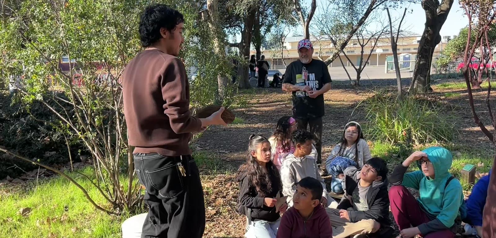 A Druids docent stands and teaches a seated circle of fourth graders in the Native Plant Forest