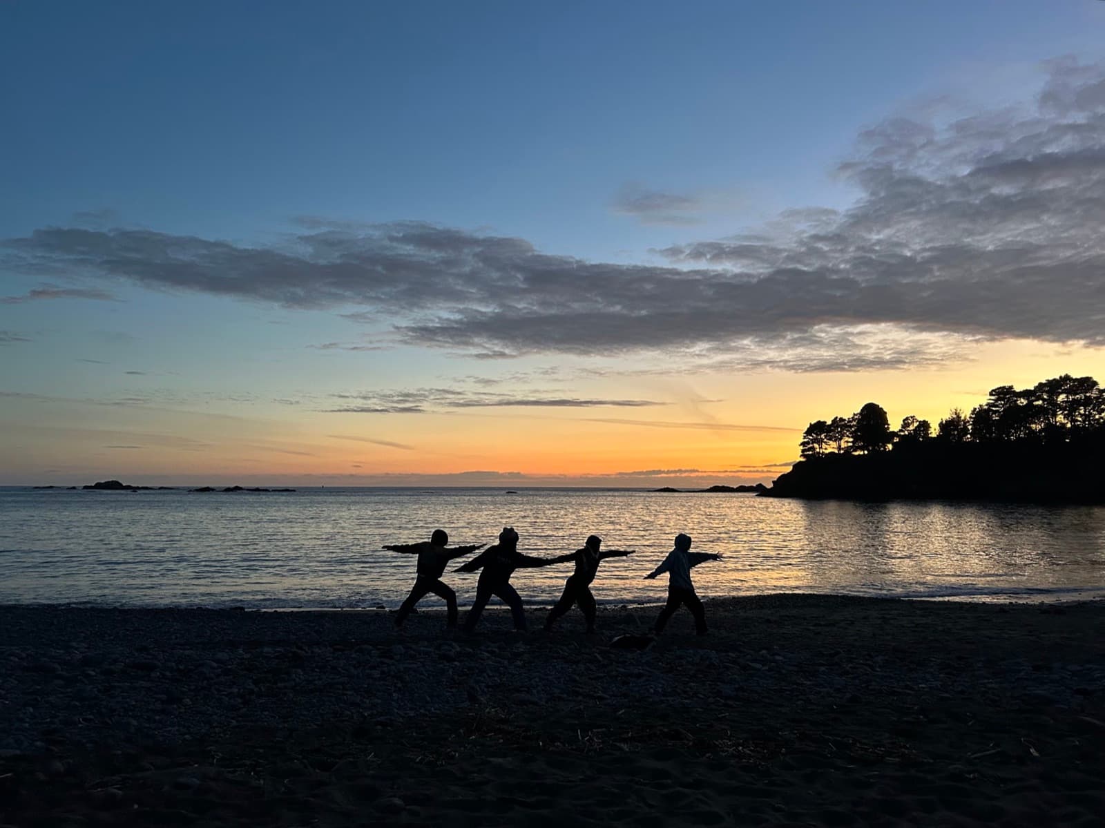 Four students play in a line, silhouetted against an orange sunset on the beach at Van Damme State Park